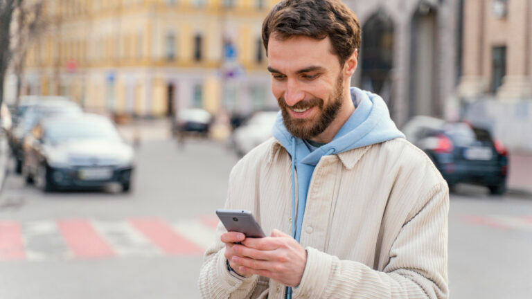 Mann steht in der Stadt und schaut auf sein Handy.