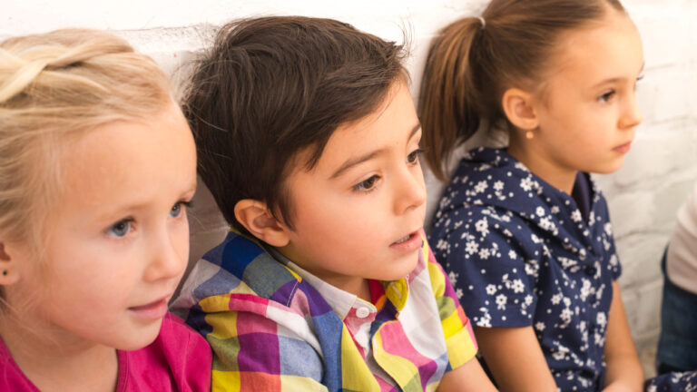 Drei Kinder sitzen nebeneinander und blicken gespannt nach rechts aus dem Bild.