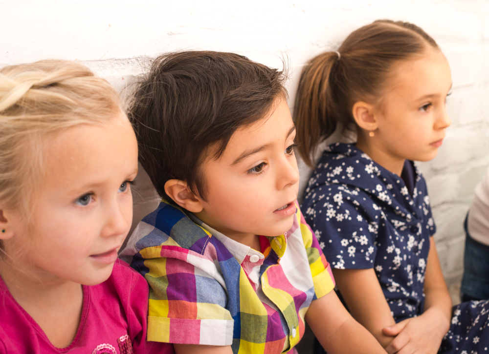 Drei Kinder sitzen nebeneinander und blicken gespannt nach rechts aus dem Bild.