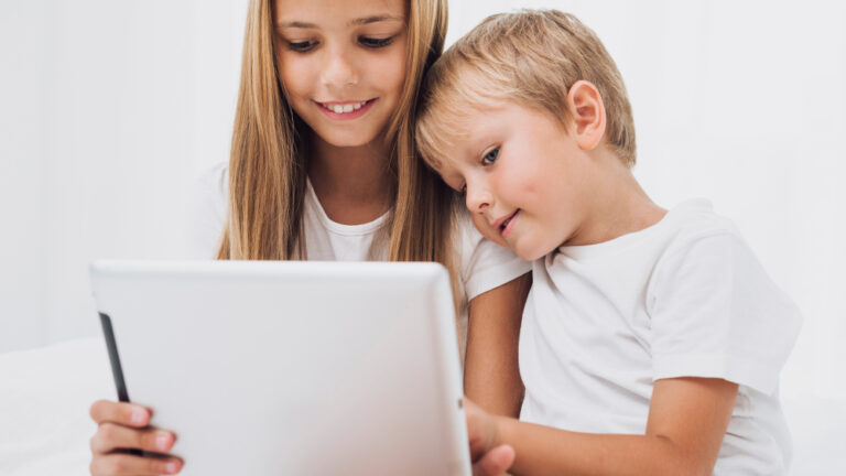 Zwei Kinder, ein Mädchen und ein kleiner Junge, schauen zusammen auf ein Tablet.