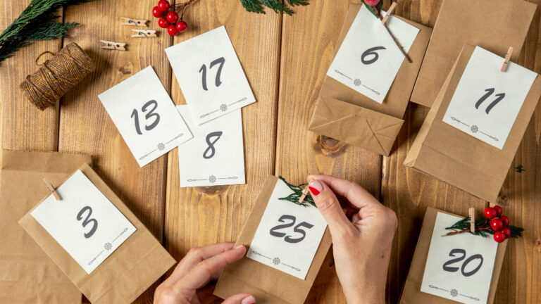 Zwei Hände befestigen eine nummerierte Karte auf einer kleinen Papiertüte für einen Adventskalender.